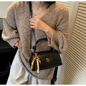 Close-up of black leather handbag featuring vintage gold lock and colorful beaded tassel