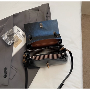 Détail du sac noir brillant avec fermoir doré, doublure rayée et bandoulière