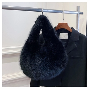 Detail of fluffy faux fur handbag in solid black hanging against a blazer backdrop