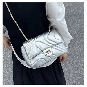Detail der silbernen Stepptasche mit Wellennähten und goldenem Drehverschluss am Gurt