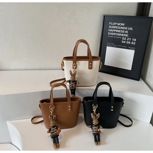 Three textured bucket bags with plaid rabbit charms and detachable straps in tiered display
