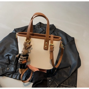 Detail of cream bucket bag with brown trim, featuring a plaid rabbit charm and lychee texture