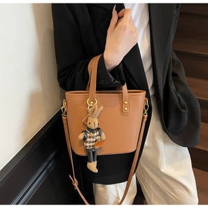 Close-up of brown pebbled leather bucket bag with gold hardware and knit rabbit charm