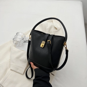 Sac seau minimaliste en cuir noir avec détails dorés présenté dans un décor de mode chic