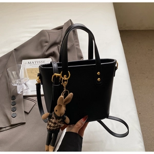 Detail of black pebbled leather tote bag with gold hardware and knit rabbit pendant decoration