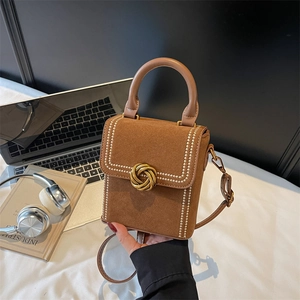 Brown suede crossbody bag with gold buckle and white stitching, shown with laptop