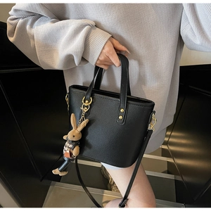 Detail of black lychee grain handbag with gold hardware and a cute rabbit charm
