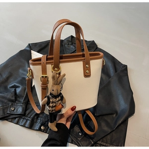 Detail of a beige bucket bag with brown trim and a cute rabbit charm on a leather jacket