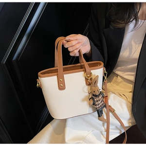 Detail view of stylish cream bucket bag with brown handles and cute rabbit plush charm