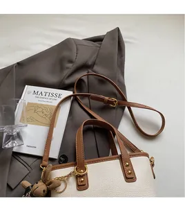 Close-up of a chic contrast tote bag with a brown plush rabbit charm and gold hardware