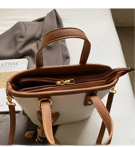 Top view detail of cream mini tote bag featuring smooth golden zipper and brown leather handles