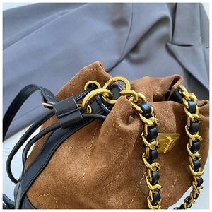 Détail du sac seau en daim marron vintage avec surpiqûres matelassées et chaîne dorée