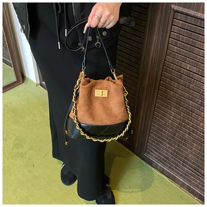 Détail du sac seau contrasté avec daim marron, cuir matelassé noir et poignée chaîne dorée