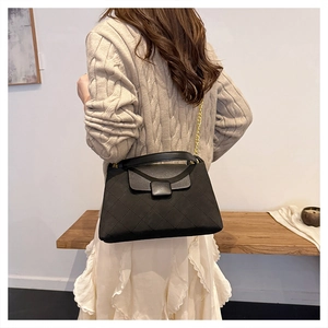 Close-up of black quilted chain bag with matte texture on a beige sweater model