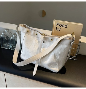 Macro detail of creamy white wrinkled leather tote with gold studs on a display stand