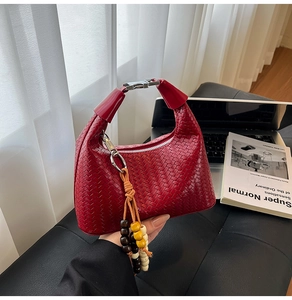 Close-up of red woven leather handbag with silver handle and wooden bead charm accessory