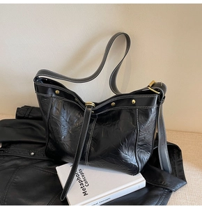 Detail of black faux leather tote bag with white stitching and vintage gold hardware