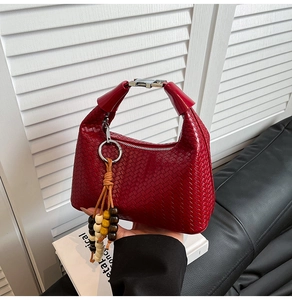 Detail of dark red woven handbag featuring silver clasp and colorful wooden bead tassel