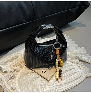 Detail of black woven handbag with wooden bead tassel and silver metallic hardware