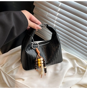 Detail of black woven leather handbag featuring a stylish wooden bead tassel and silver zipper