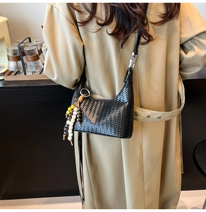 Detail of black woven shoulder bag with a decorative wooden bead tassel on a beige trench coat