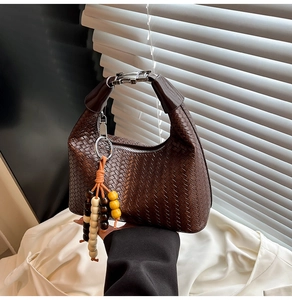 Detail of dark brown woven leather handbag with silver buckle and beaded tassel charm