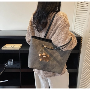 Detailed texture of grey tote bag with soft plush bear charm and sleek black straps