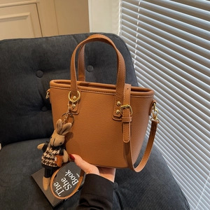Brown lychee leather bucket bag with top handles and a cute bunny doll charm on a sofa