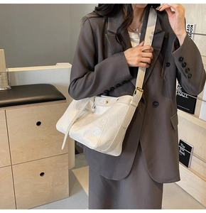 Detail of white vintage pleated shoulder bag with gold clasp on a gray blazer