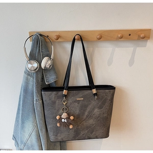 Detail of dark grey tote bag with metal logo, plush charm and casual lifestyle styling