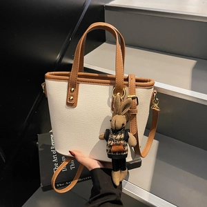 Elegant white leather bucket bag with brown trim and cute rabbit pendant on stairs