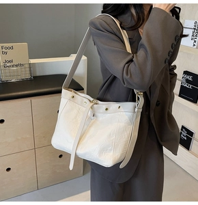 Chic off-white leather tote bag with metallic buckles worn by a model in modern setting