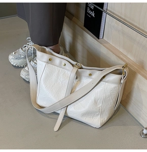 Close-up of cream leather tote bag featuring natural pleated texture and gold metal rivets