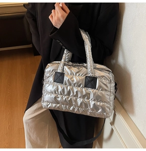 Detail of silver quilted puffer tote bag with metallic finish and black strap on model