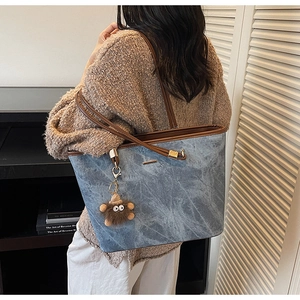 Detail of blue-gray textured tote bag with brown straps and plush monster charm