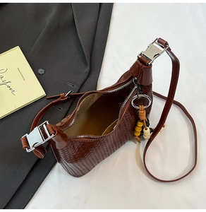 Detail of dark brown woven shoulder bag featuring metallic buckle and beaded tassel charm
