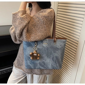 Detail of blue denim tote bag with brown leather straps and a plush monster charm