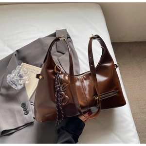 Détail du sac hobo en cuir marron foncé avec poche zippée et bandoulière réglable sur fond blanc