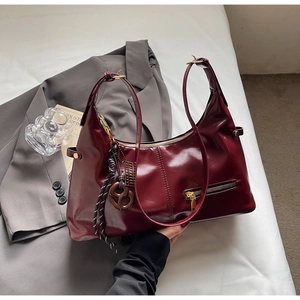 Gros plan détaillé du sac à bandoulière en cuir verni rouge foncé et ferrures en métal