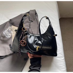Détail du sac demi-lune noir brillant avec fermeture éclair dorée et breloque marron