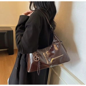 Détail du sac hobo bordeaux brillant avec zip doré et breloque en cuir noué