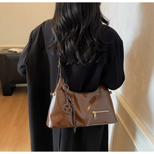 Détail du sac à bandoulière en cuir verni marron foncé avec fermeture éclair dorée et bijou