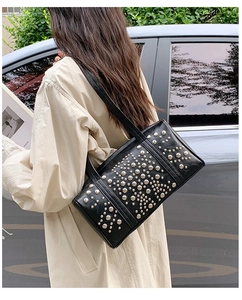 Detail view of black glossy leather underarm bag with silver stud accents on model