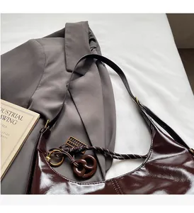 Détail du sac hobo en cuir verni marron foncé avec nœud tressé et breloque anneau
