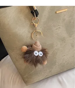 Close-up of a creative brown plush monster charm with mini knit hat on a green handbag