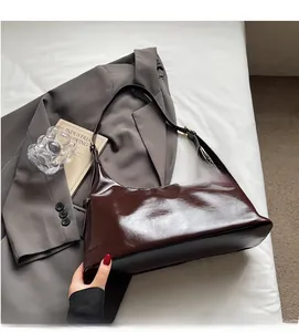 Détail du sac bandoulière en cuir verni chocolat sur costume gris et livres