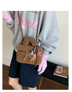Detail of plush brown mini tote bag featuring teddy bear charm and stars on white wall