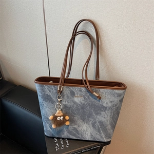 Detail of blue denim tote bag with brown leather handles and plush bear charm
