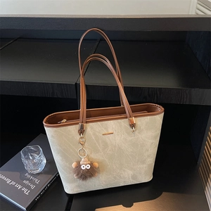 Close-up of beige tote bag showing textured surface, brown leather trim and plush charm