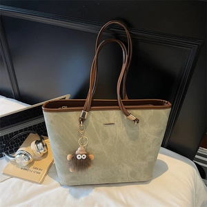 Detail of light green marble-textured tote bag with plush monster charm on a white bed